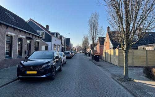Foto van straat met links geparkeerde auto's en rechts bomen