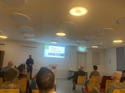 Presentatie op de muur met daarvoor mensen op stoelen die naar deze presentatie kijken